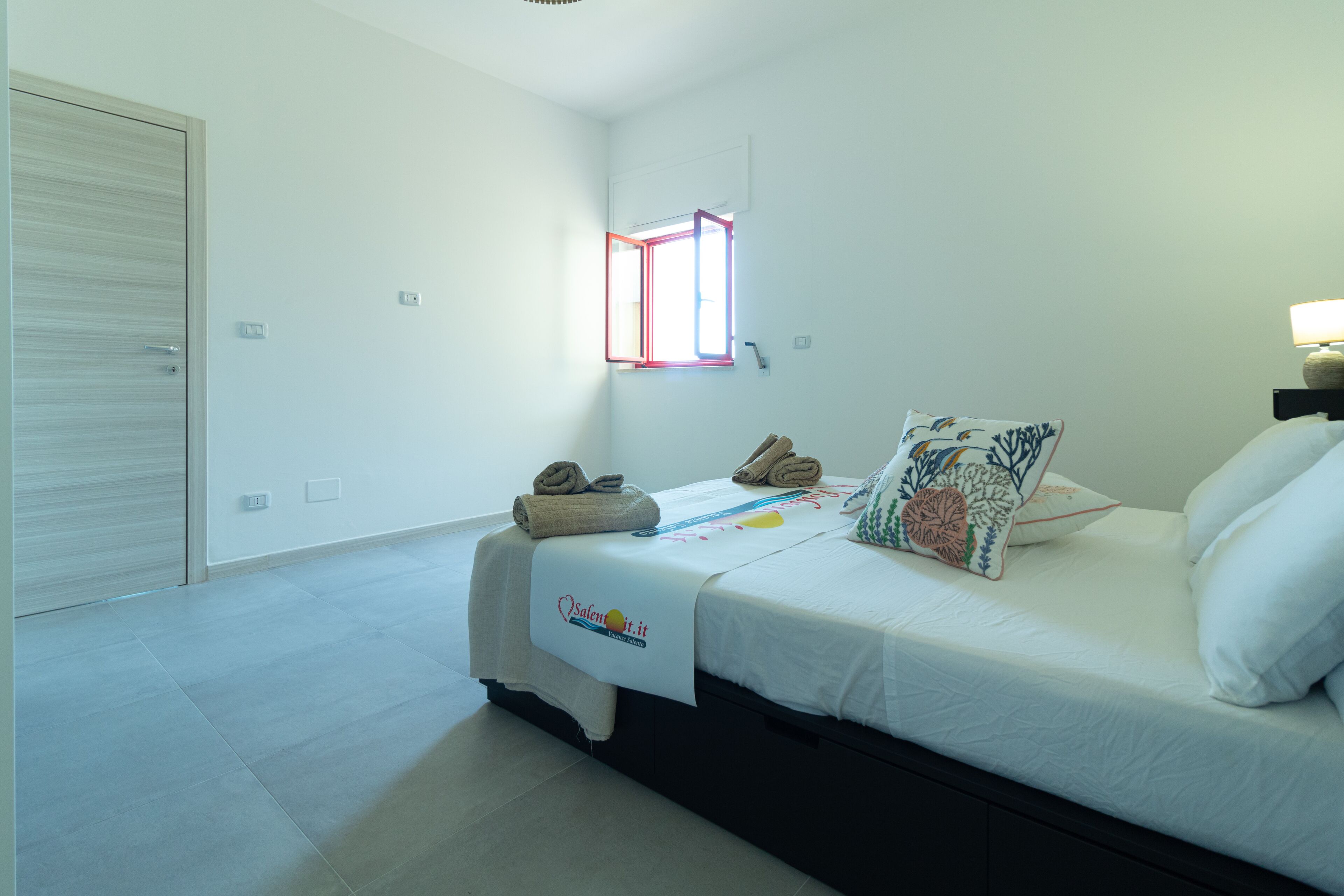 Ein Schlafzimmer mit Bett, Fenster, Nachttisch und Tür.