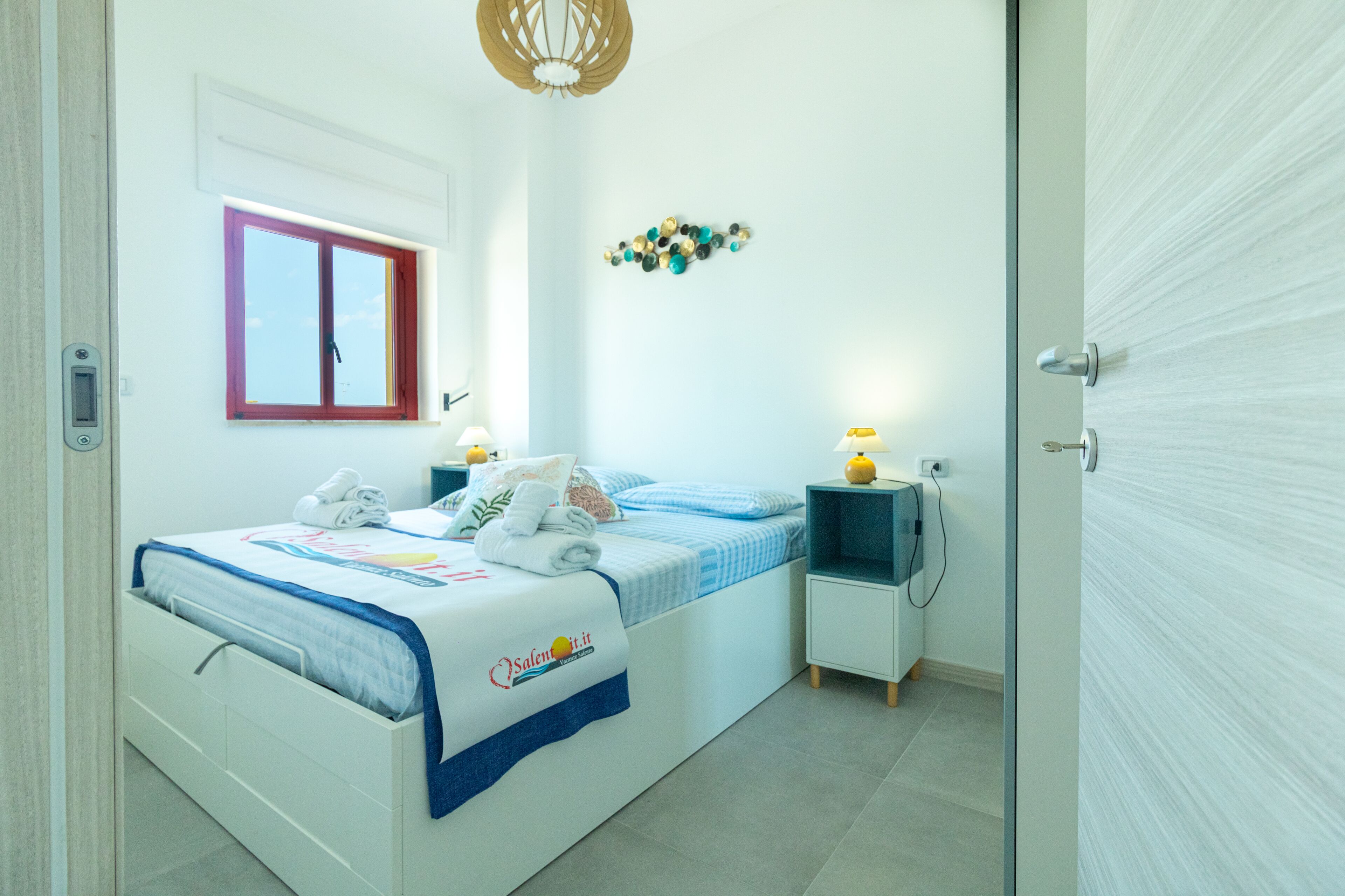 A bedroom with a bed, bedside tables, a window, and a wall decoration.