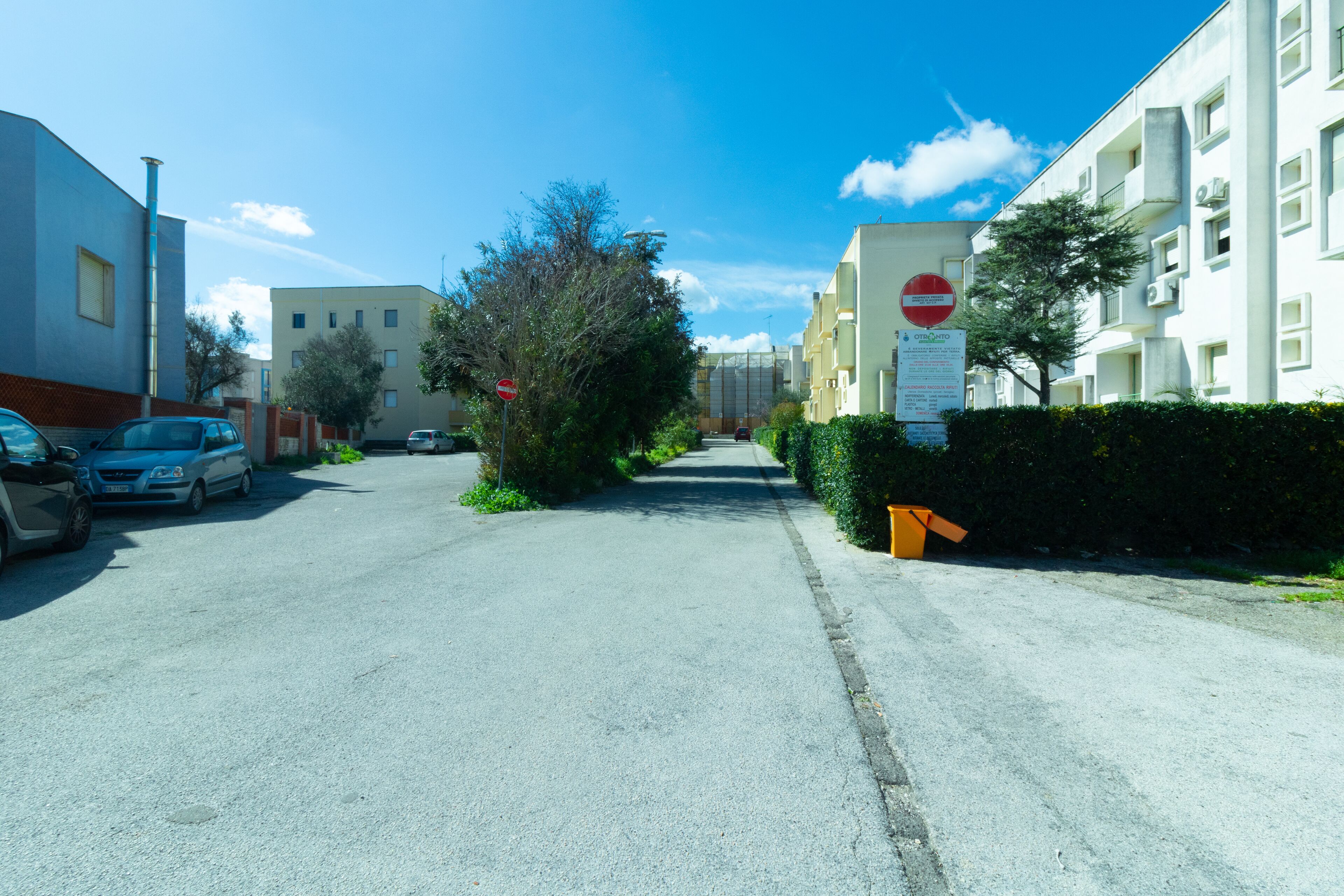 Una calle residencial con coches estacionados, una señal de prohibido el paso y edificios de apartamentos.