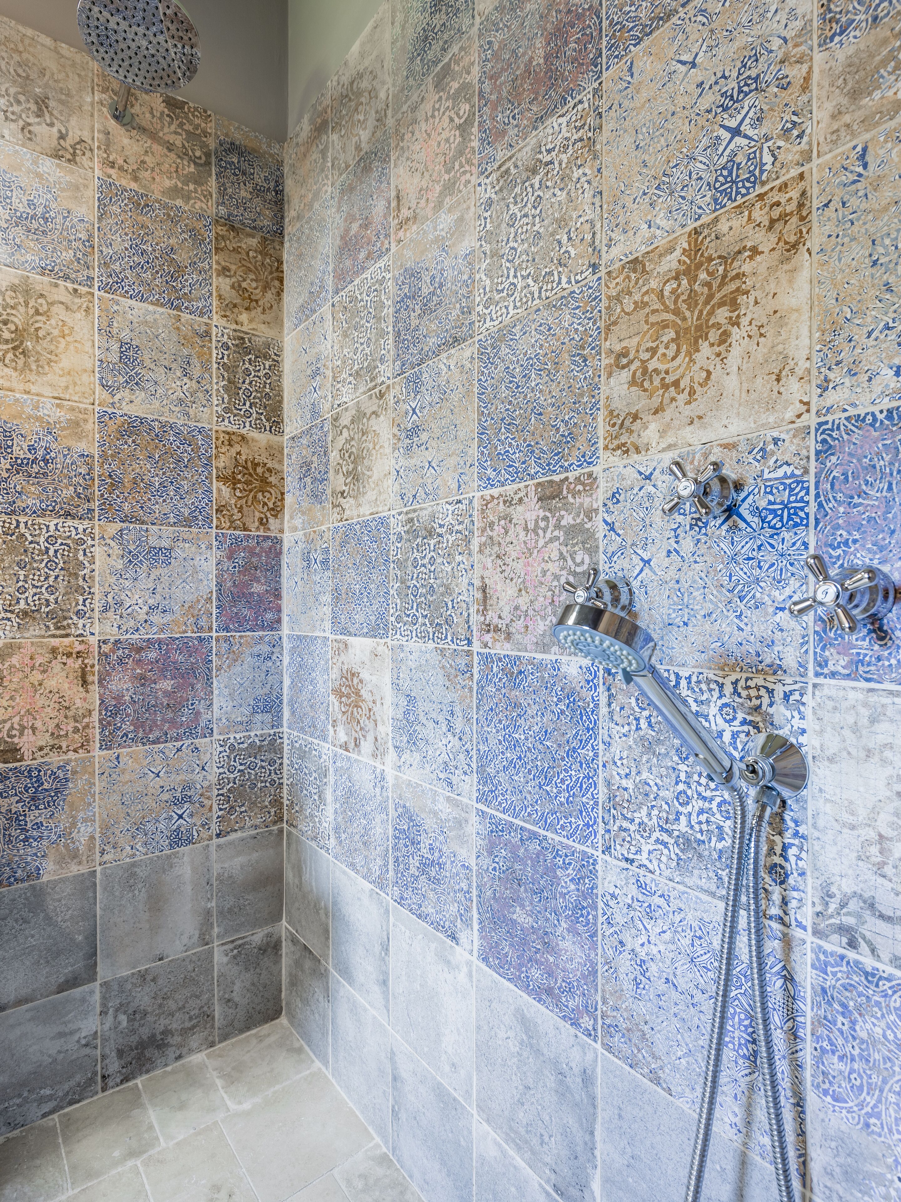 Un espacio de ducha con azulejos decorativos y un cabezal de ducha de mano.
