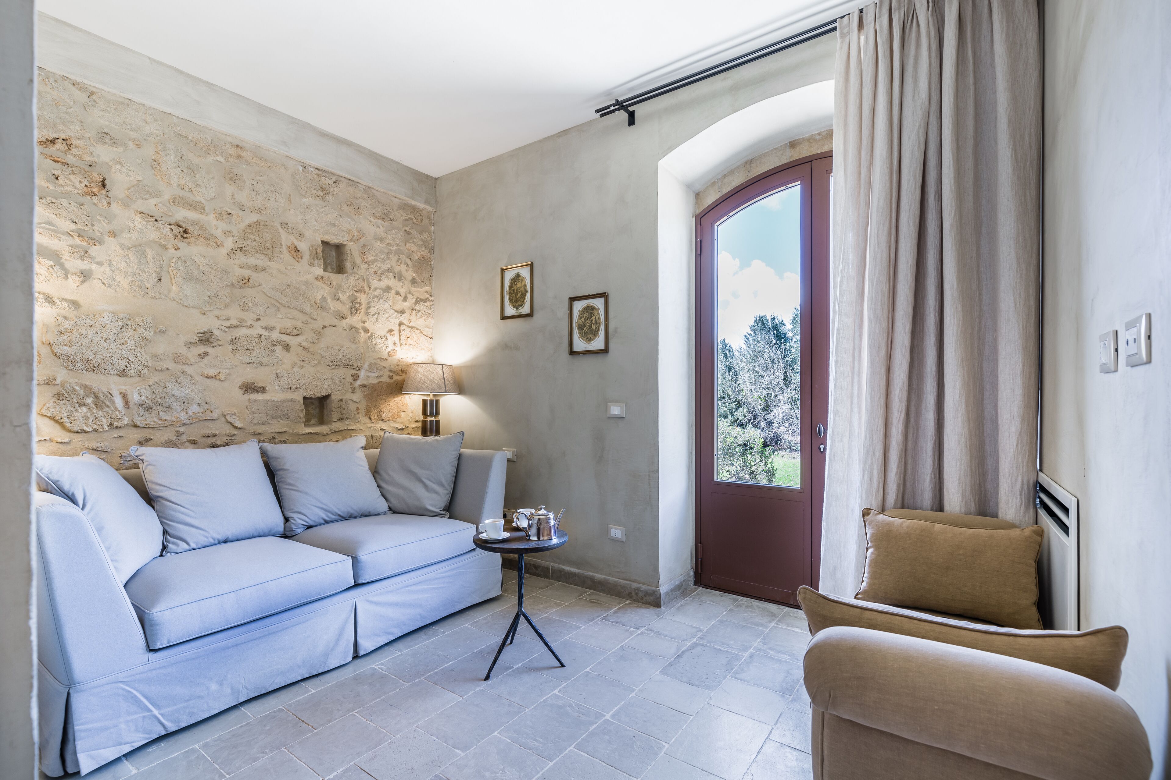 A living room with a stone wall, a sofa, a chair, a small table, and a door with curtains.