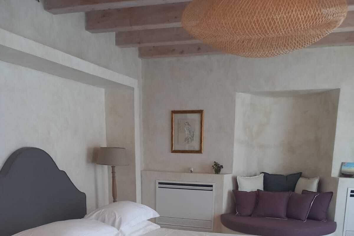 Quarto com cama, mesa de cabeceira, luminária, sofá e quadro na parede.