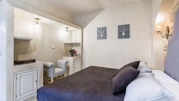 Un dormitorio con cama, una silla, una mesita pequeña y una estantería en la pared.