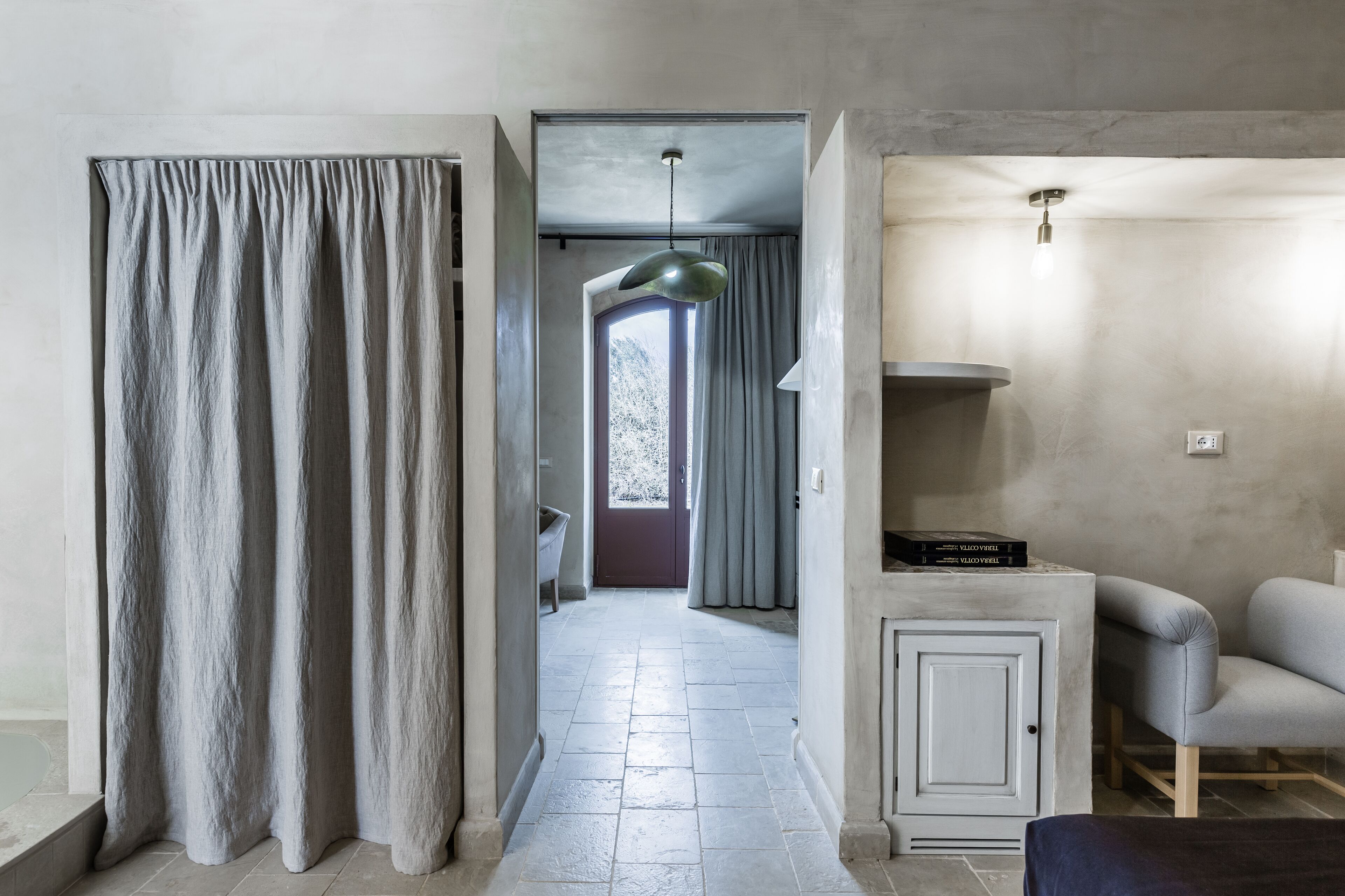 Un pasillo con una cortina gris, una lámpara, un armario y una silla.