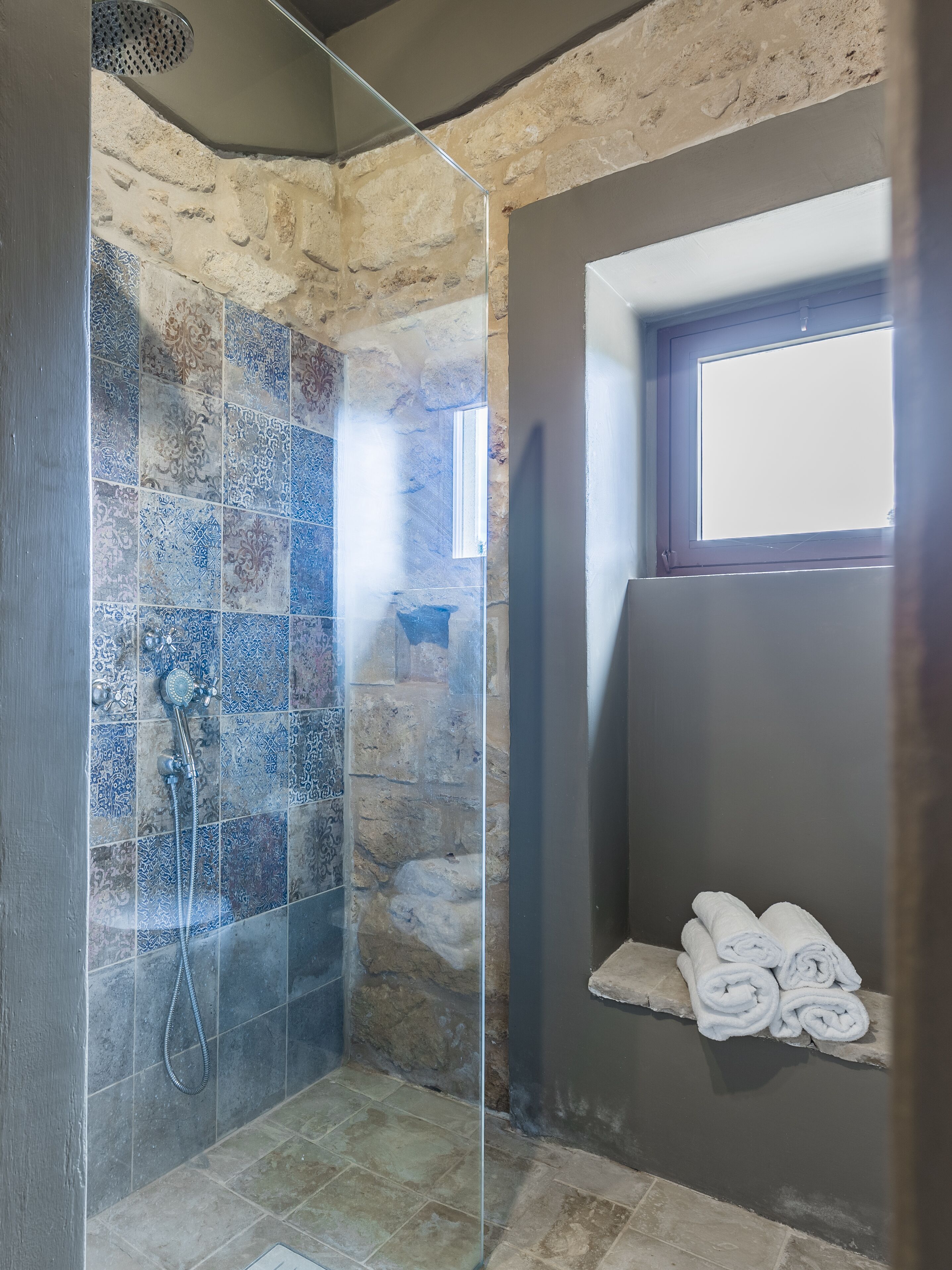 Una ducha con azulejos estampados, una puerta de cristal y un perchero con toallas.