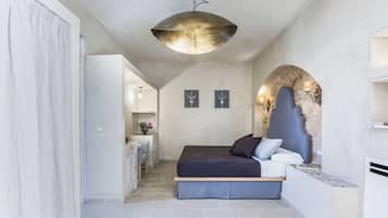 Quarto com cama, luminária pendente, arco de pedra e pequena escrivaninha com cadeira.
