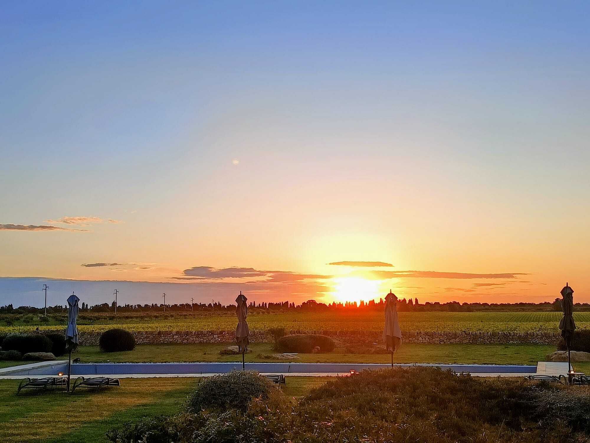 Ein Sonnenuntergang über einem Feld mit einer Straße, einer Steinmauer und einigen Stühlen.