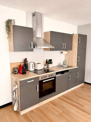 A modern kitchen with grey cabinets, a stainless steel range hood, a built-in oven, and a wooden countertop. - JUPAS° Boho Home – Balcony, Parking & Playground (Trier)