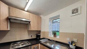 A modern kitchen with wooden cabinets, a built-in oven, a dishwasher, and a window with a view of greenery. - Tastefully Decorated 1 bed Flat Near Abbeywood (Belvedere)