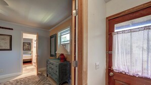 A hallway with a wooden door, a window with lace curtains, a dresser with a lamp, and a framed picture on the wall. - Latitude Adjustment - Ocracoke Island (Ocracoke)