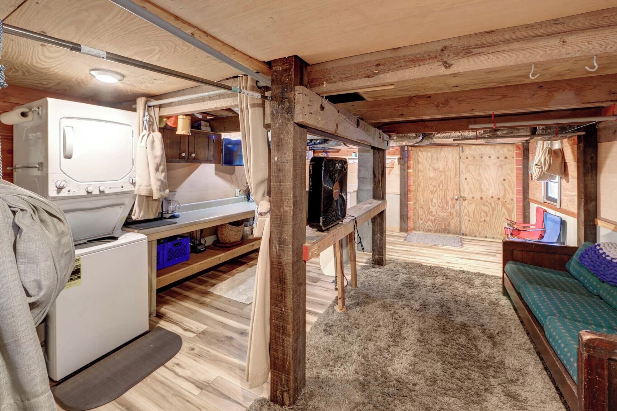 A compact, rustic room with a washing machine, a fan, and a bed.
