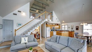 A spacious living area with a staircase leading to an upper level, a kitchen with wooden cabinets, and a dining area with a table and chairs. - Heart's Desire - Ocracoke Island (Ocracoke)