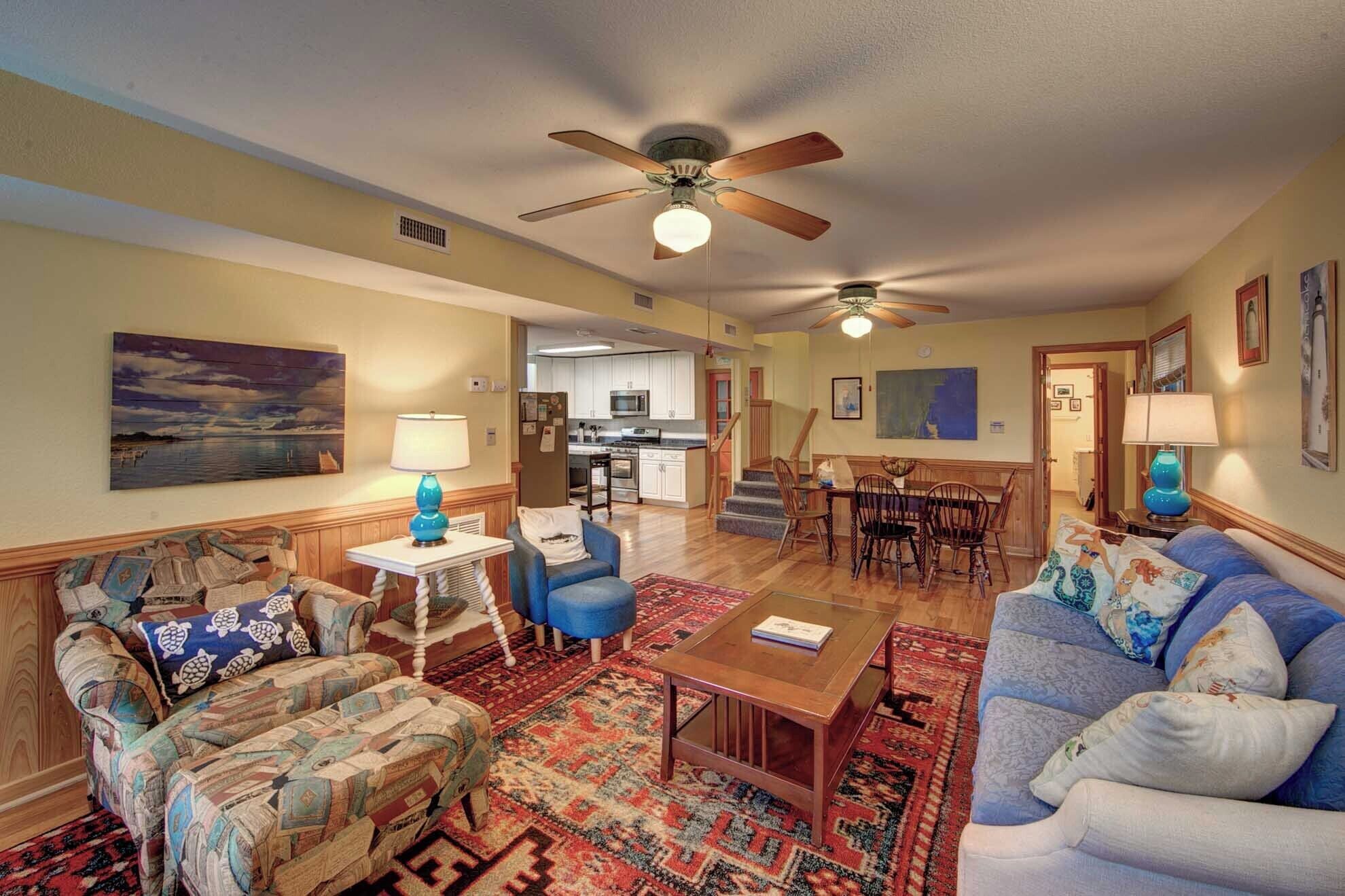 A living room with a blue sofa, a patterned armchair, a coffee table, and a dining area with a wooden table and chairs.