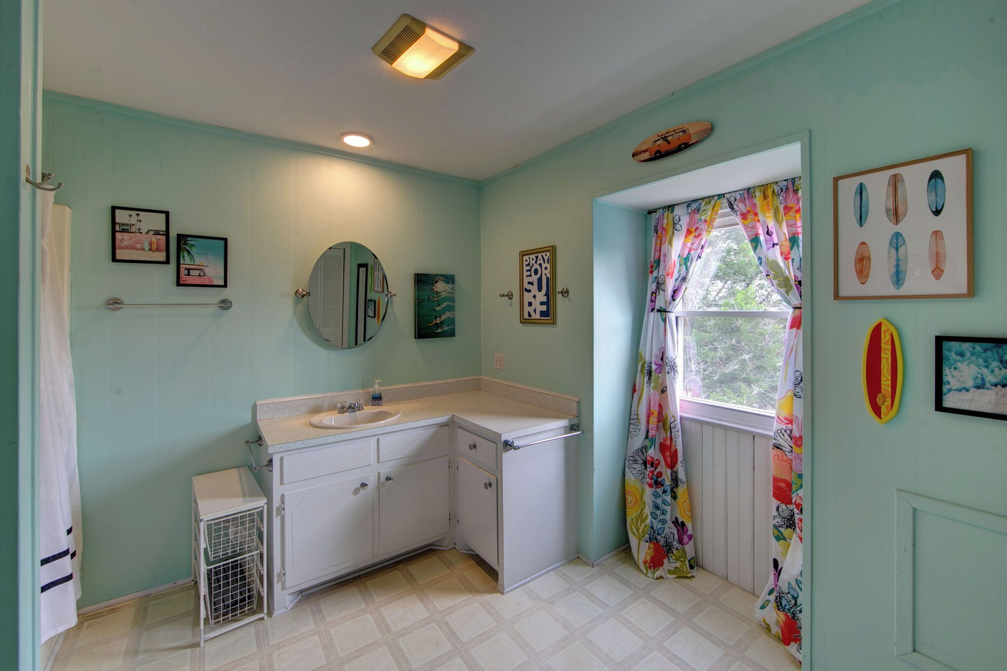A bathroom with a sink, mirror, and a window with colorful curtains.
