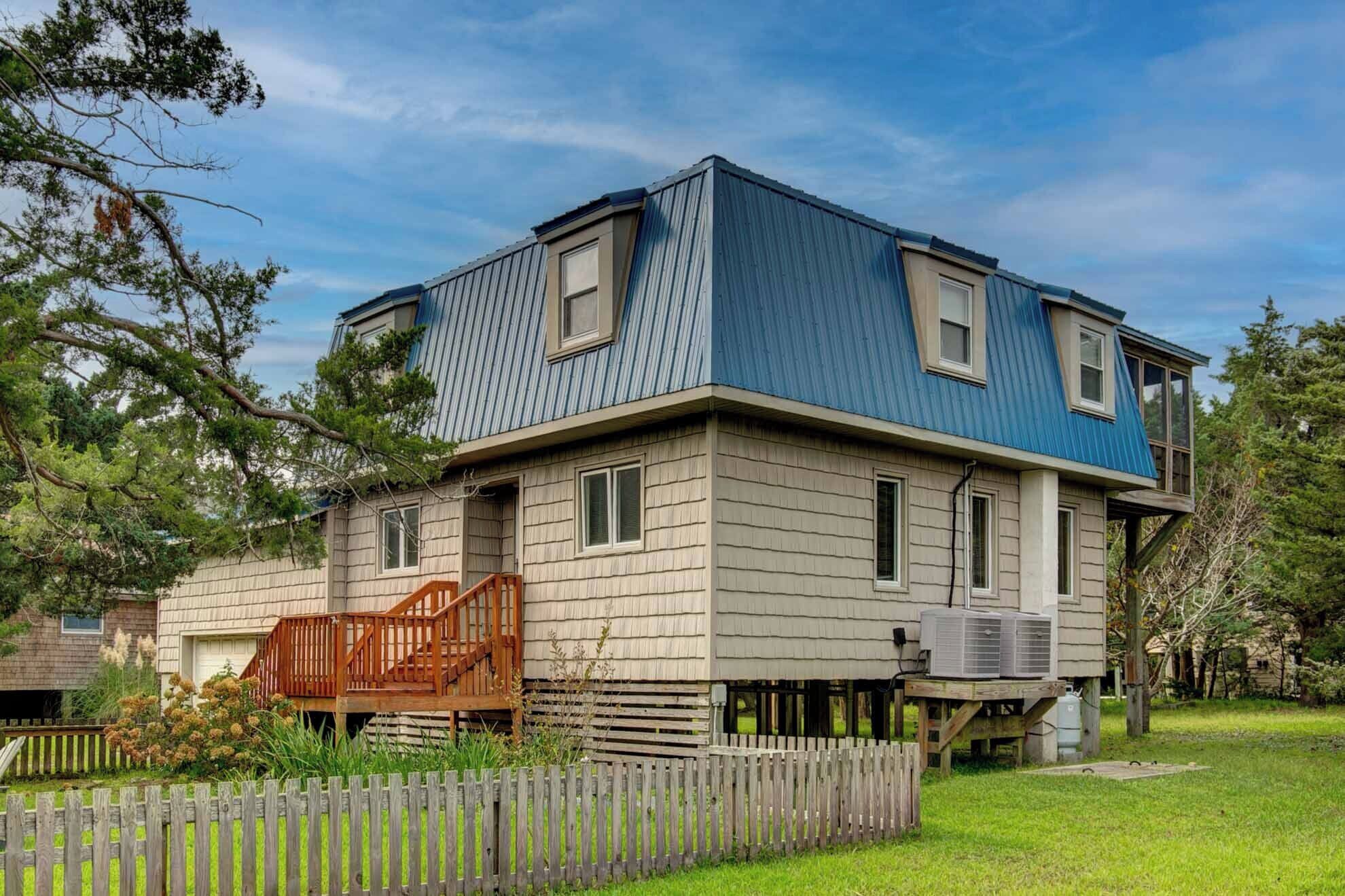 A two-story house with a blue roof, a wooden front porch, and a fenced yard.