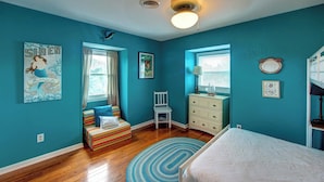 A bedroom with teal walls, a wooden floor, a bed, a window with curtains, a chair, a dresser, and a ceiling fan. - Siren Song - Ocracoke Island (Ocracoke)