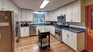 A kitchen with white cabinets, a stainless steel refrigerator, a microwave, a stove, and a sink. - Siren Song - Ocracoke Island (Ocracoke)
