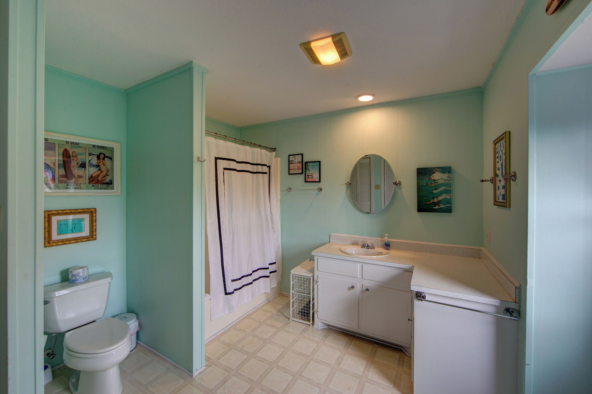 Un bagno con WC, lavandino e tenda da doccia. Alle pareti ci sono quadri incorniciati e uno specchio sopra il lavandino.