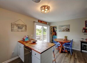 A kitchen with a wooden countertop, a dining area with blue chairs, and a ceiling light fixture.