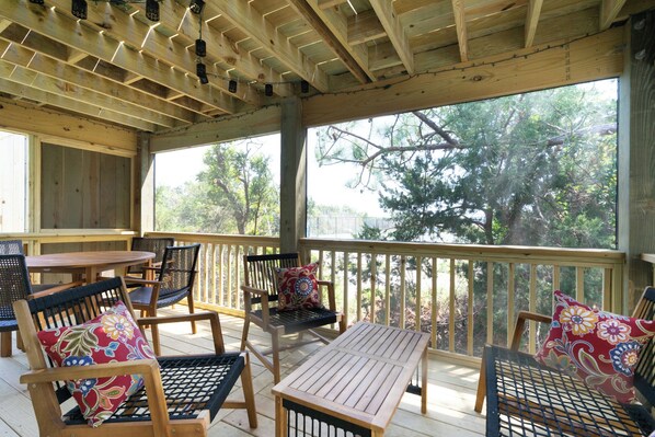 Une terrasse extérieure couverte, aménagée avec du mobilier en bois et offrant une vue sur les arbres.