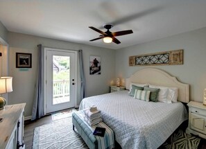 A bedroom with a bed, a ceiling fan, a nightstand, a lamp, and a door leading to an outdoor area.