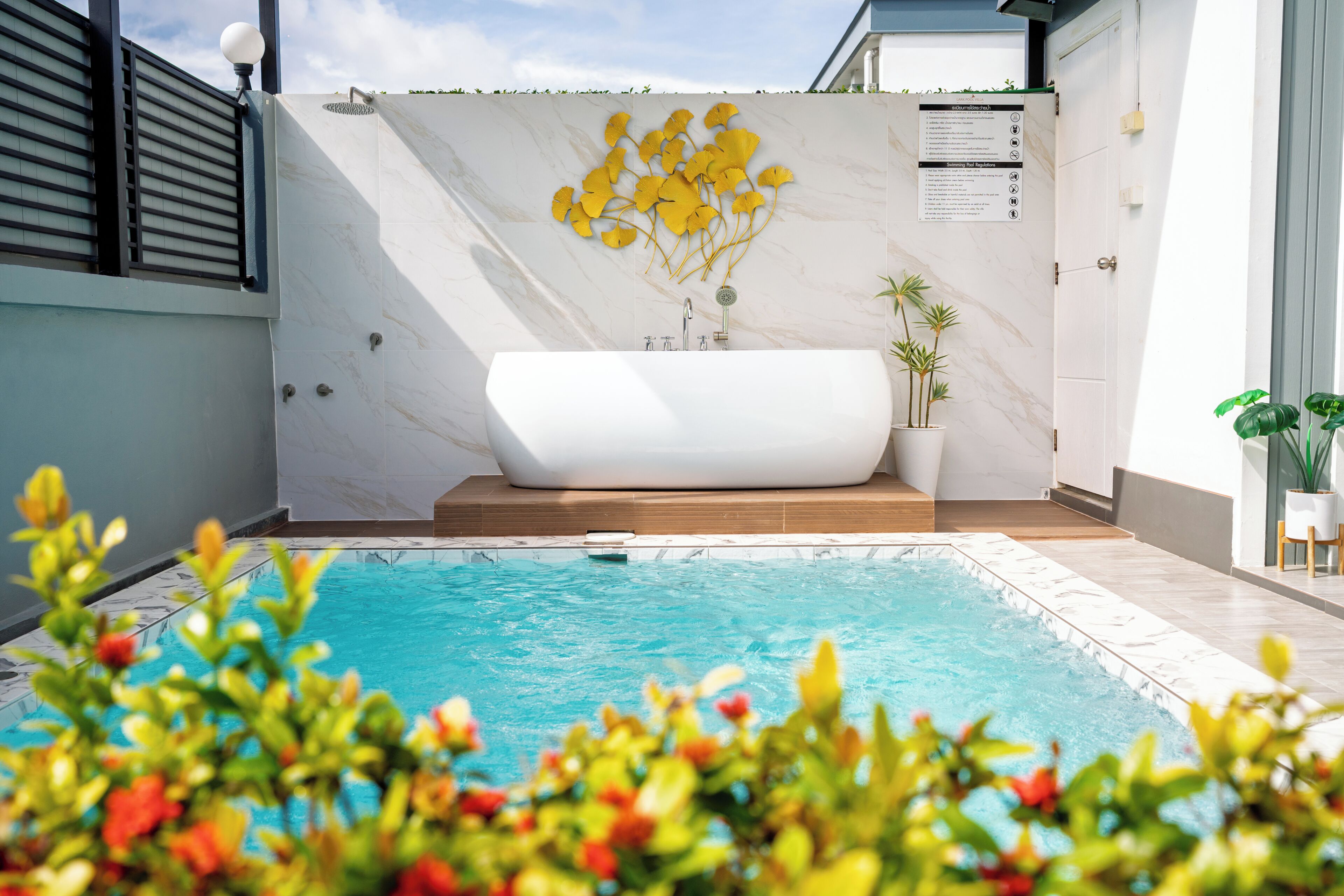 A modern outdoor pool area with a spa tub, a wall with a ginkgo leaf mural, and a poolside seating area.