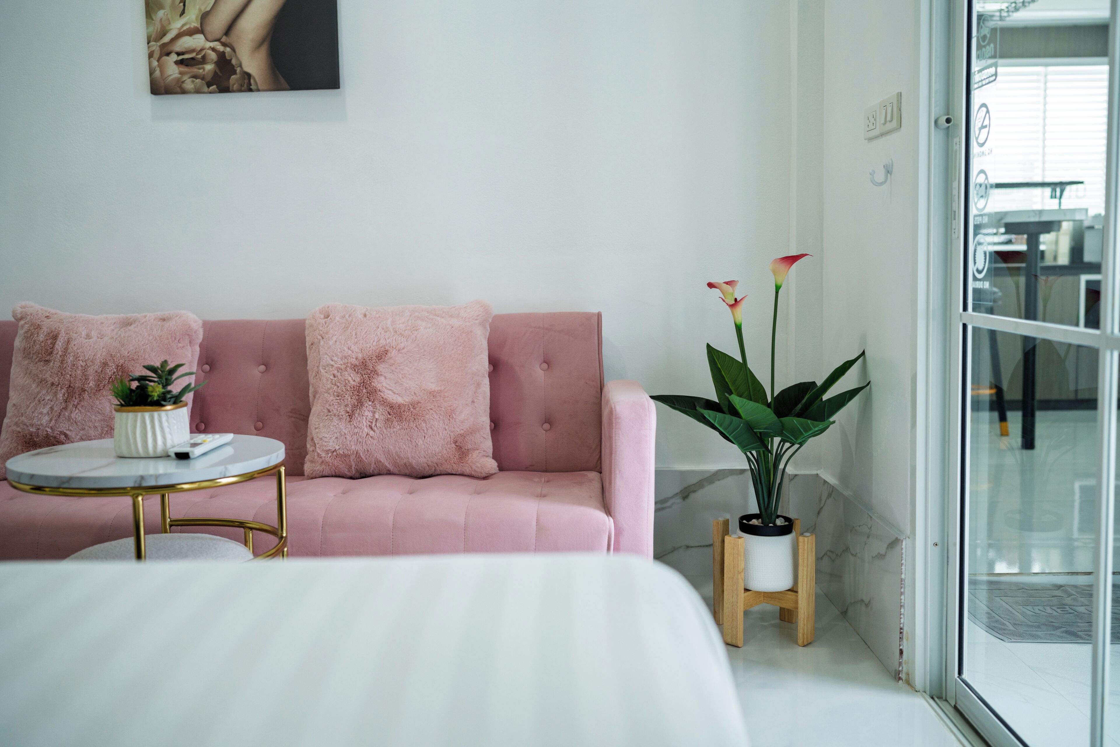 Una habitación con una cama, un sofá rosa, una pequeña mesa redonda con una planta y otra planta en maceta al lado del sofá.