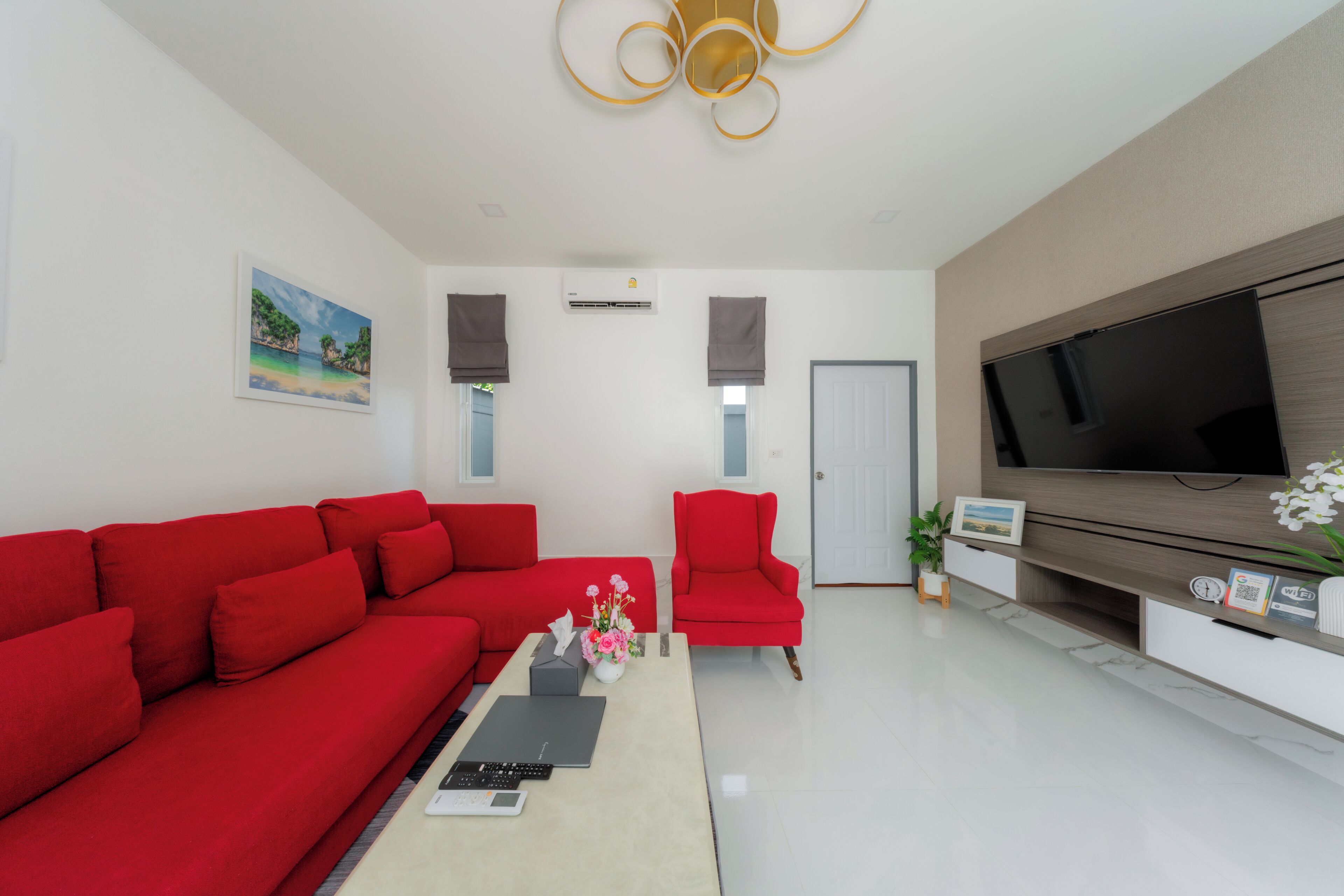 A modern living room with a red sofa, a red armchair, a flat-screen TV, and a painting on the wall.