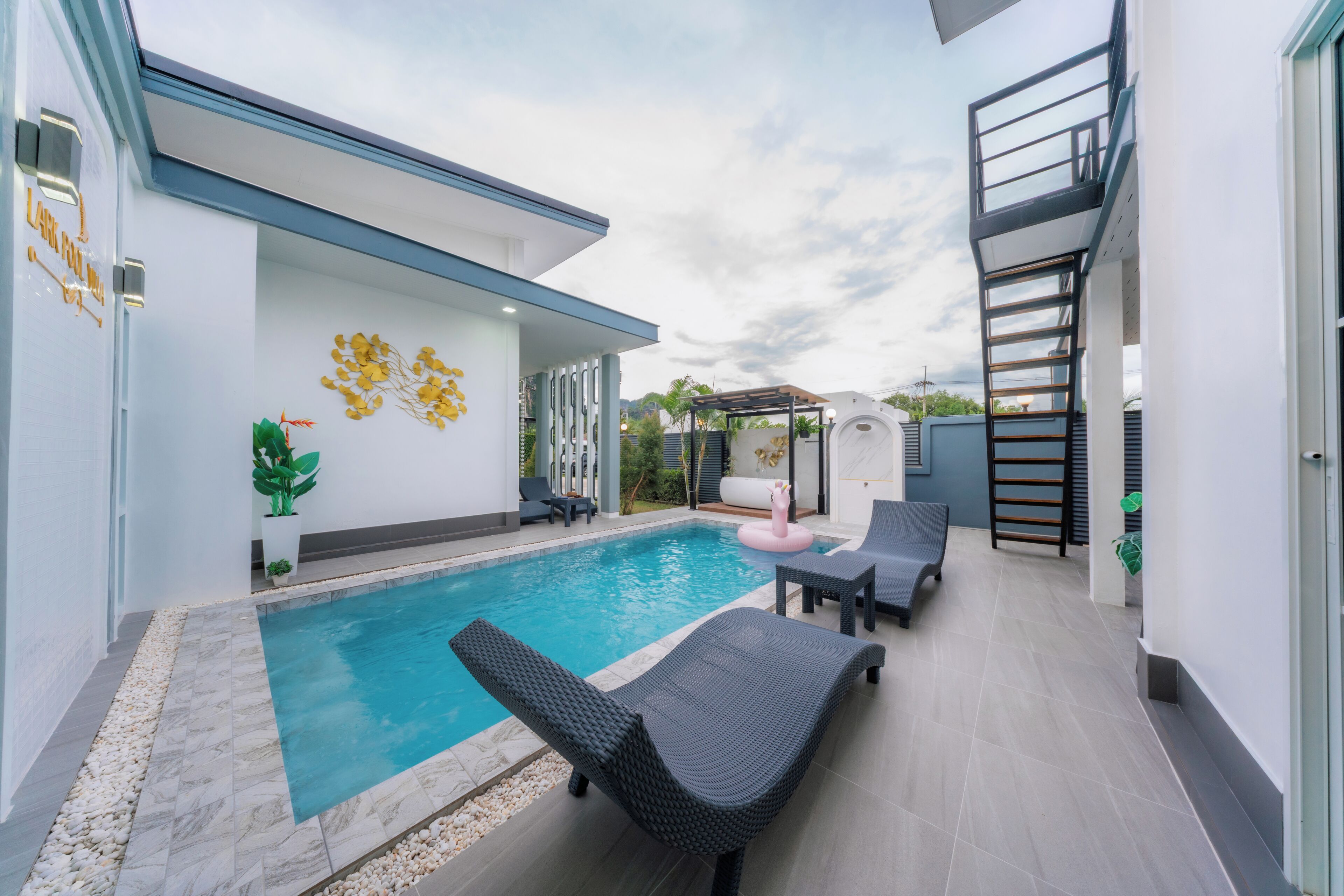 A modern outdoor pool area with lounge chairs, a decorative wall, and a pergola.