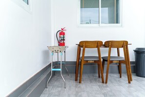 A corner with two wooden chairs, a small table, and a red fire extinguisher against a white wall. - Lark Pool Villa Krabi (Krabi)