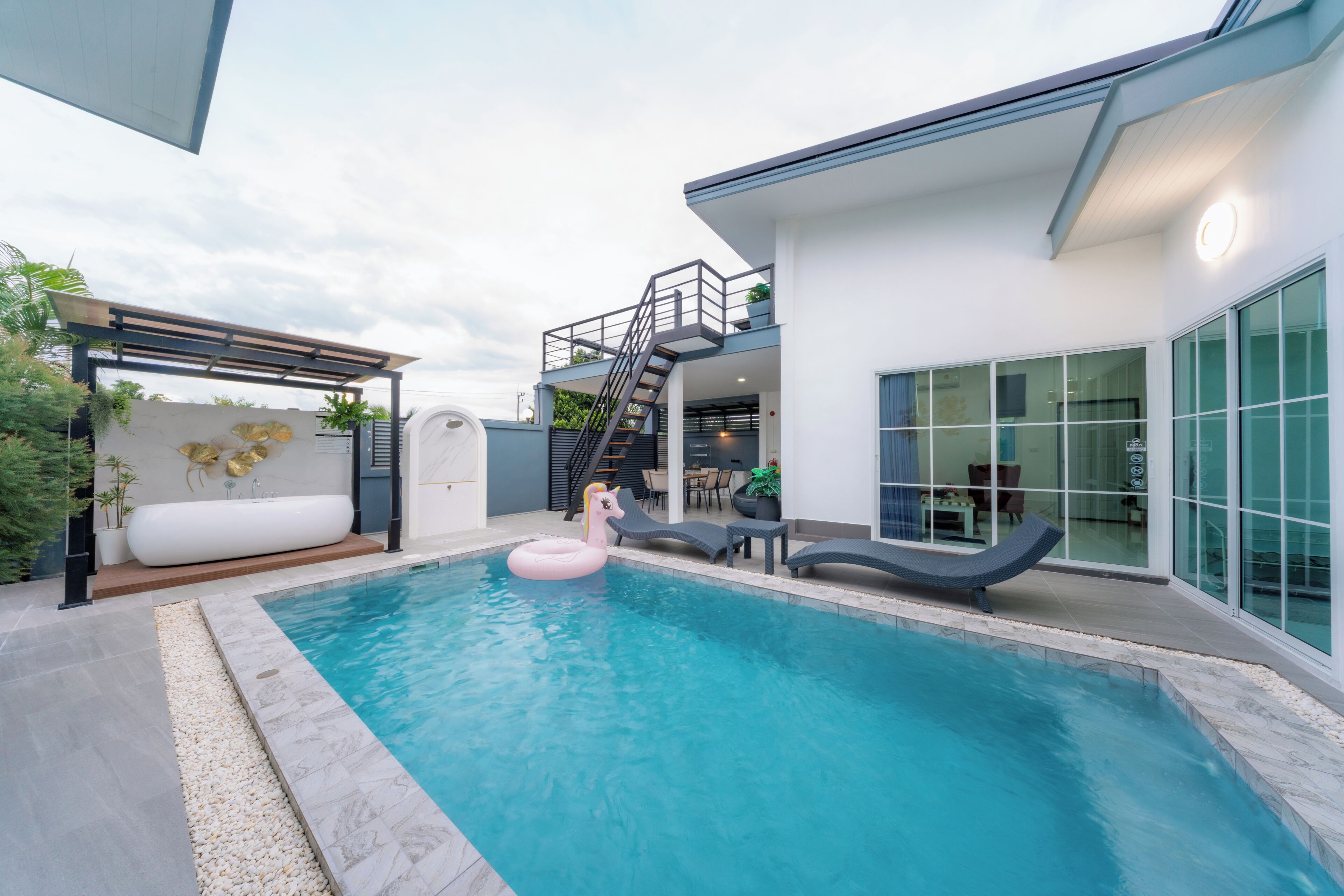 A modern outdoor swimming pool with a slide, lounge chairs, and a decorative unicorn float.