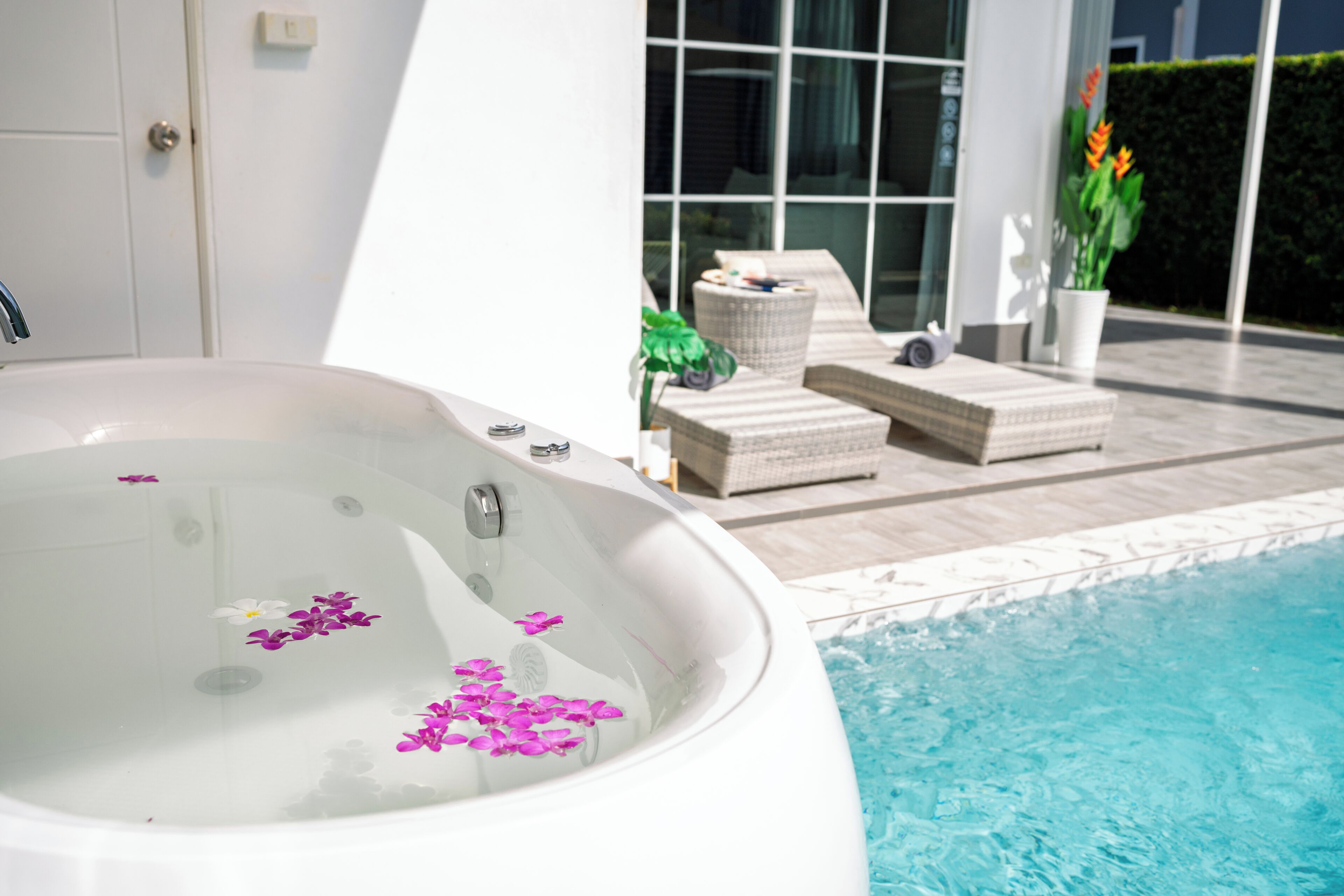A hot tub with flowers floating on the water, a pool, and lounge chairs.