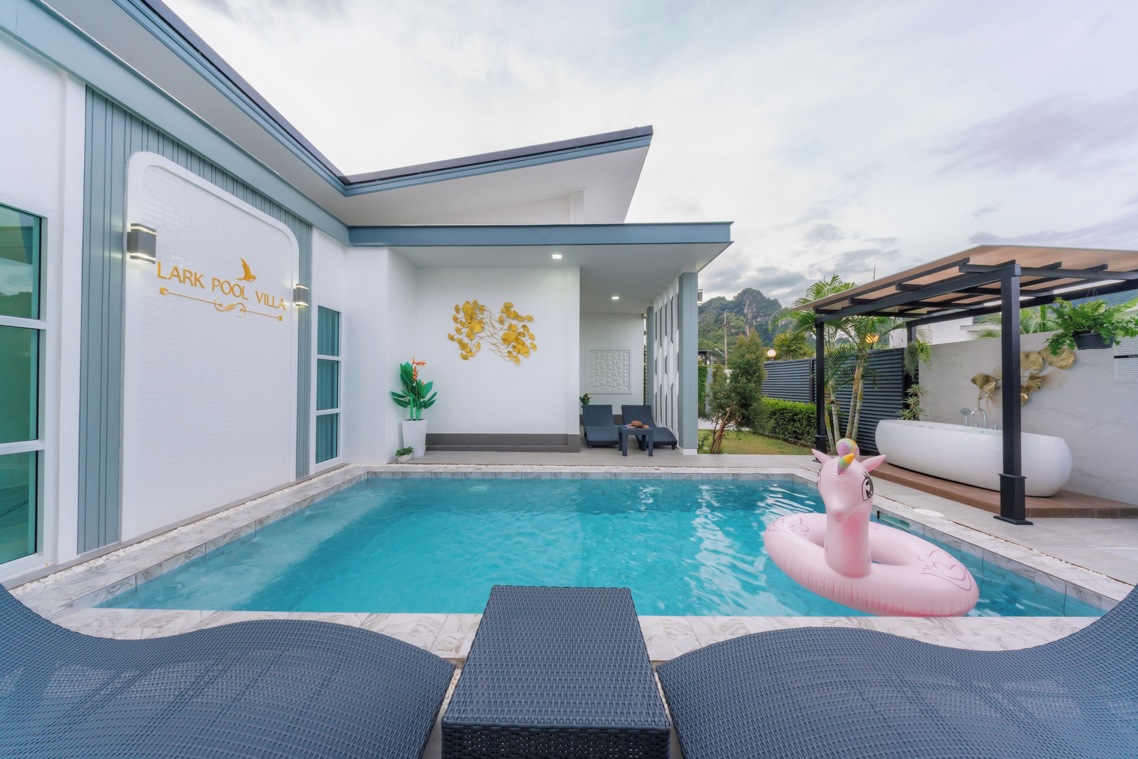A modern villa with a swimming pool, lounge chairs, and a decorative wall.