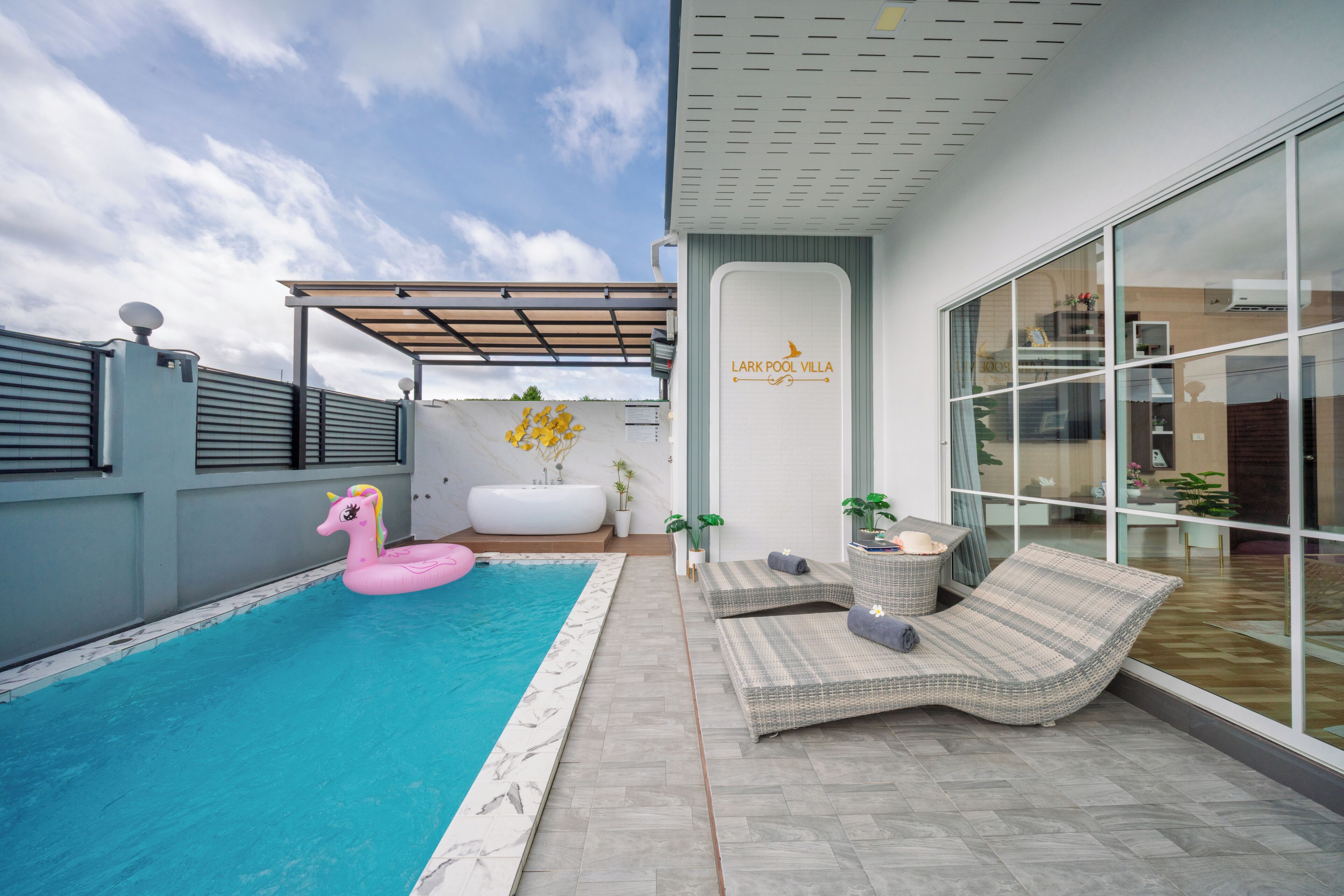 A modern pool area with a pink inflatable unicorn, a white bathtub, and lounge chairs.