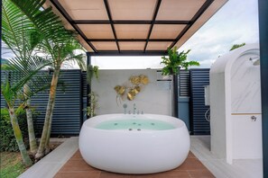 A spa area with a large bathtub, a wall-mounted shower, and a pergola with plants.