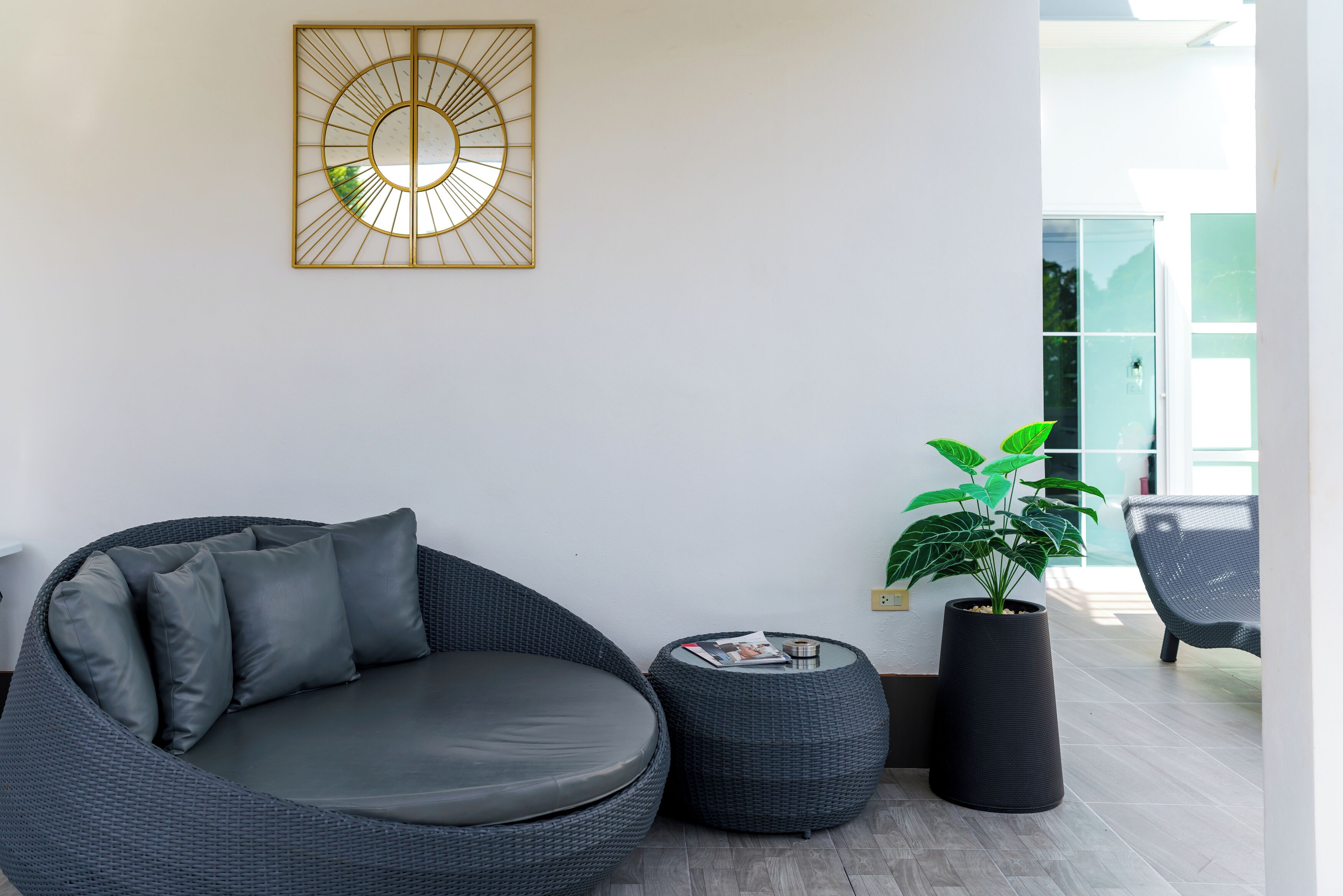 A modern living room with a dark wicker sofa, a round coffee table, a potted plant, and a decorative wall piece.