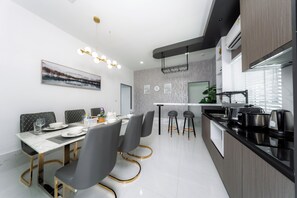 A modern kitchen with a black countertop, stainless steel appliances, and a dining area with a marble table and grey chairs.