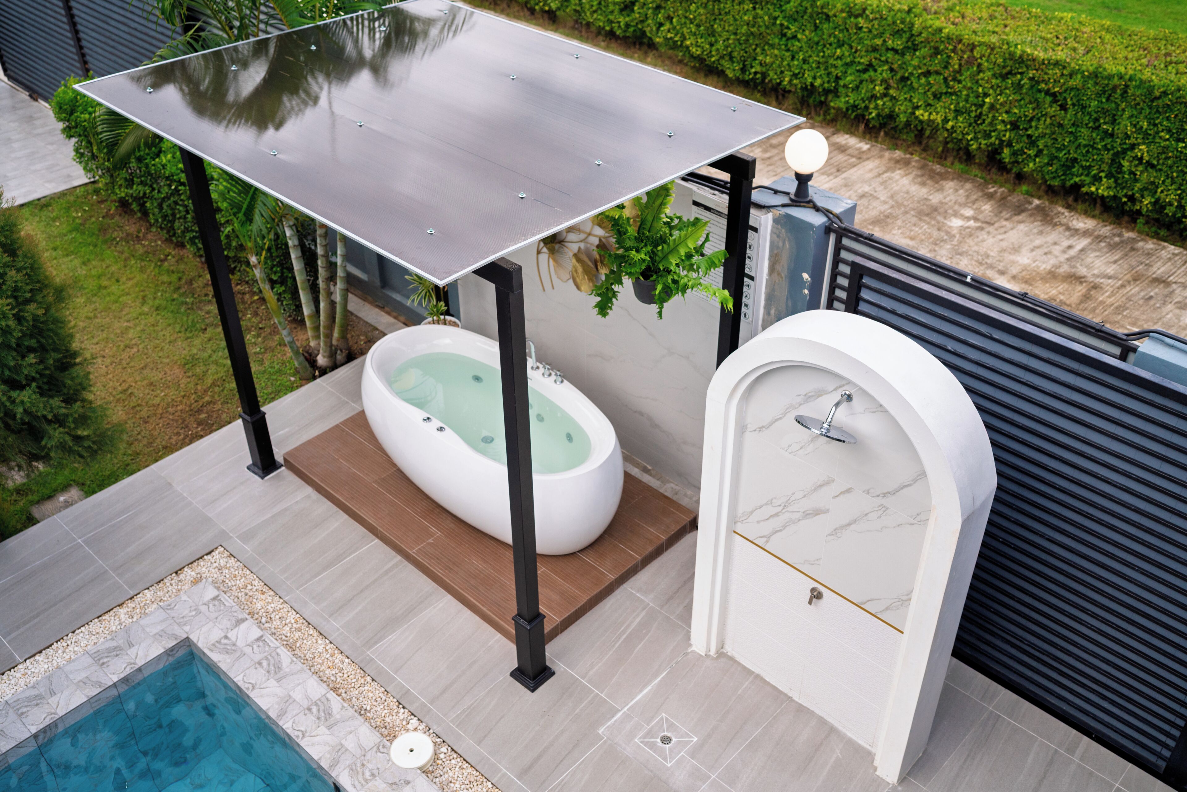 A modern outdoor bathroom with a hot tub, a shower, and a pool.