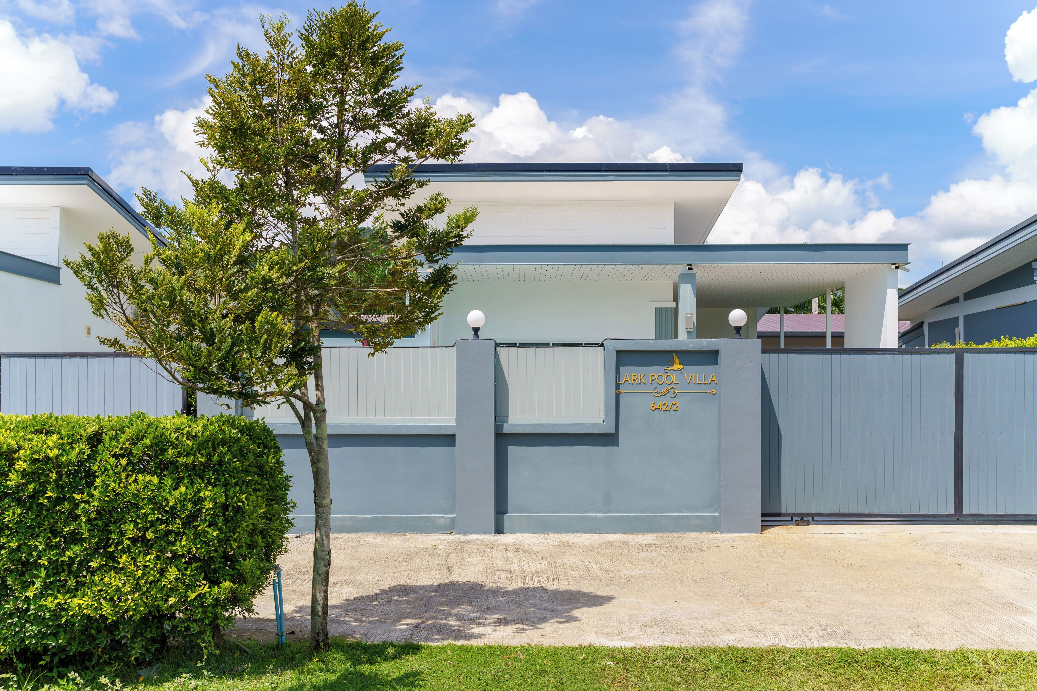A modern building with a gated entrance, a sign reading "LARK POOL VILLA," and a well-maintained lawn with a tree.