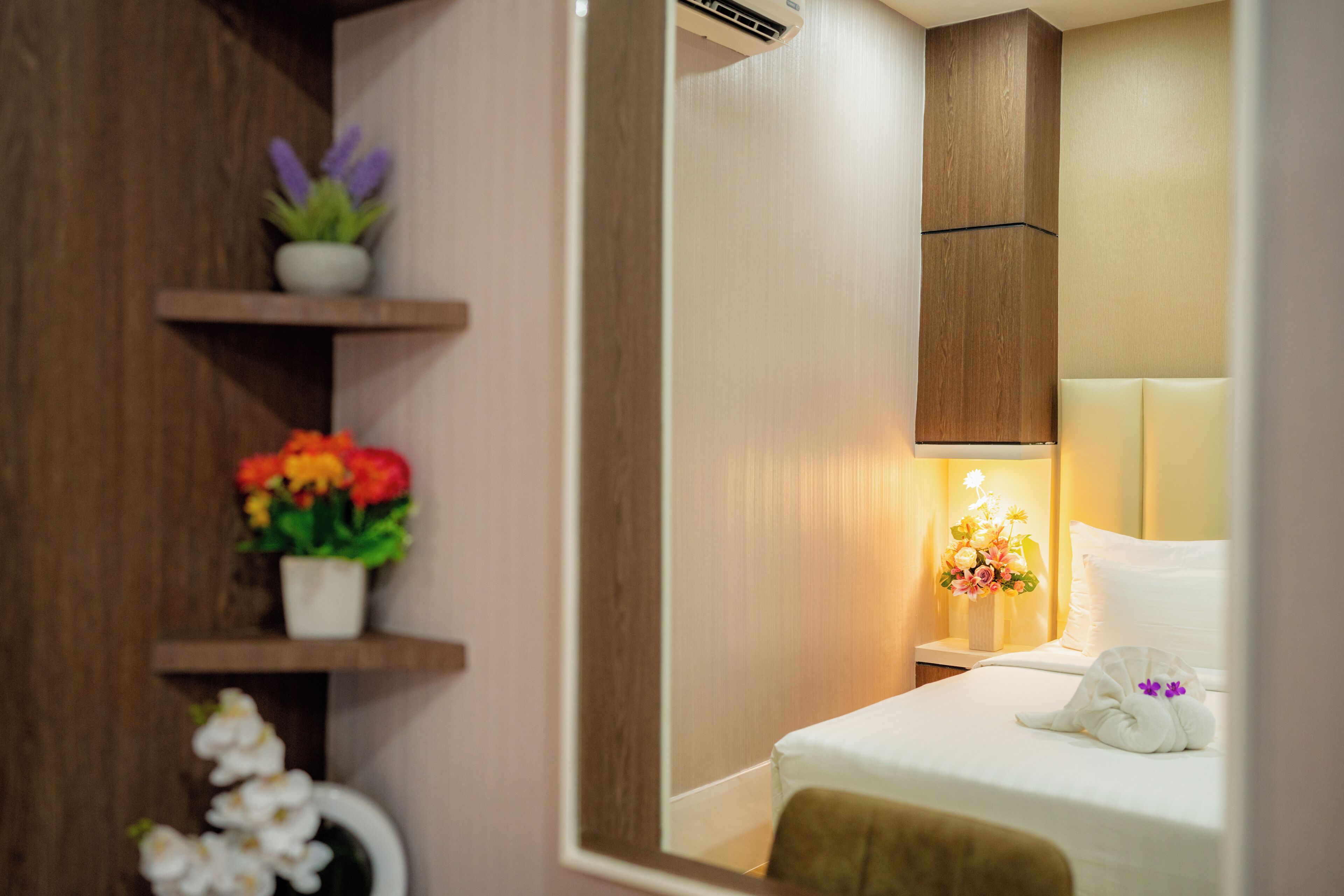Una habitación de hotel con una cama, una mesita de noche, un espejo y un estante de madera decorado con objetos.