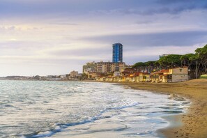 A coastal cityscape with a beach, buildings, and a prominent blue tower. - Holiday apartment mit Klimaanlage und Außenpool (Follonica)