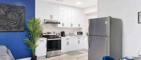 A modern kitchen with white cabinets, stainless steel appliances, a blue accent wall, and a dining area with a blue chair.