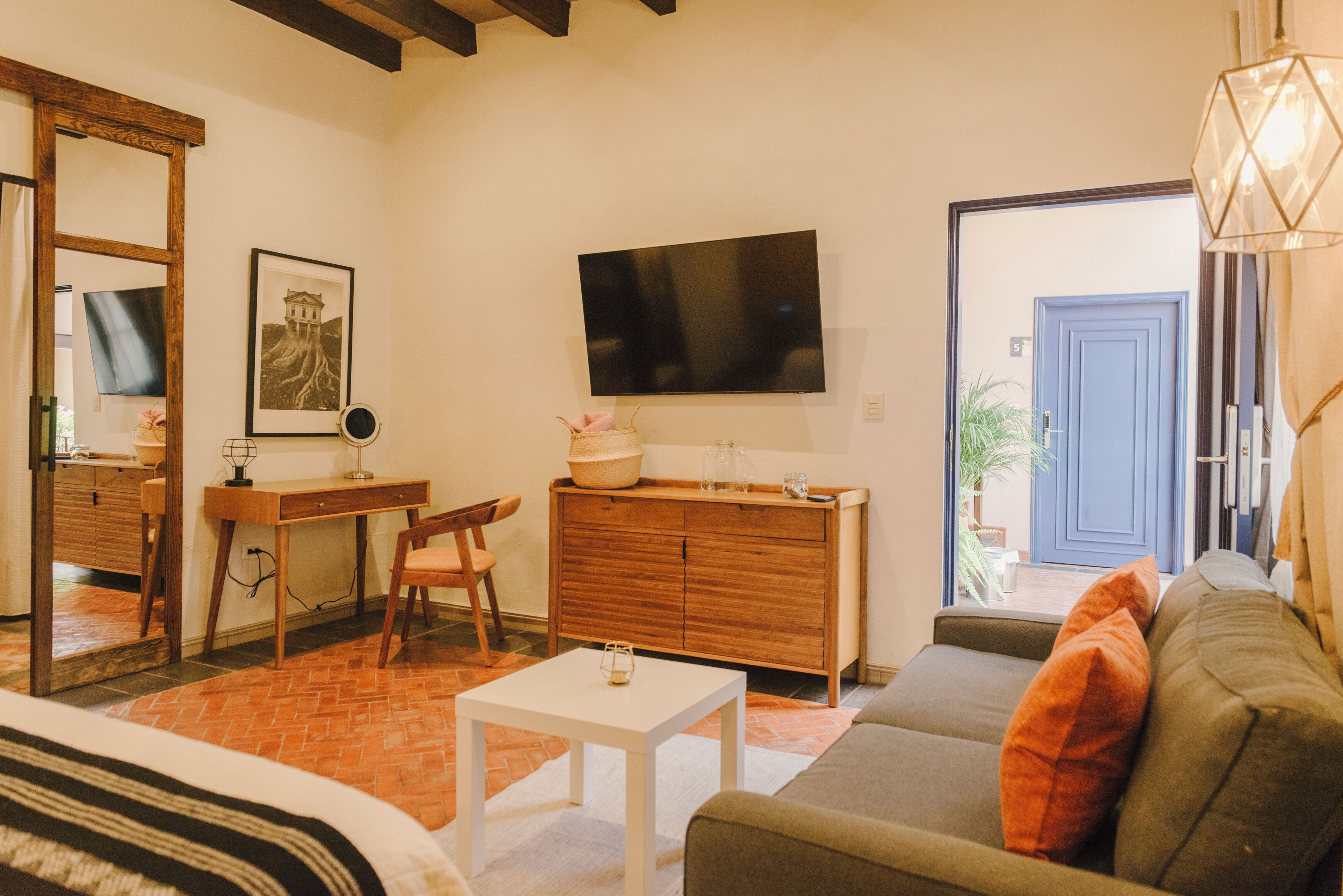 A living room with a sofa, a small table, a wooden desk, a television, and a mirror.