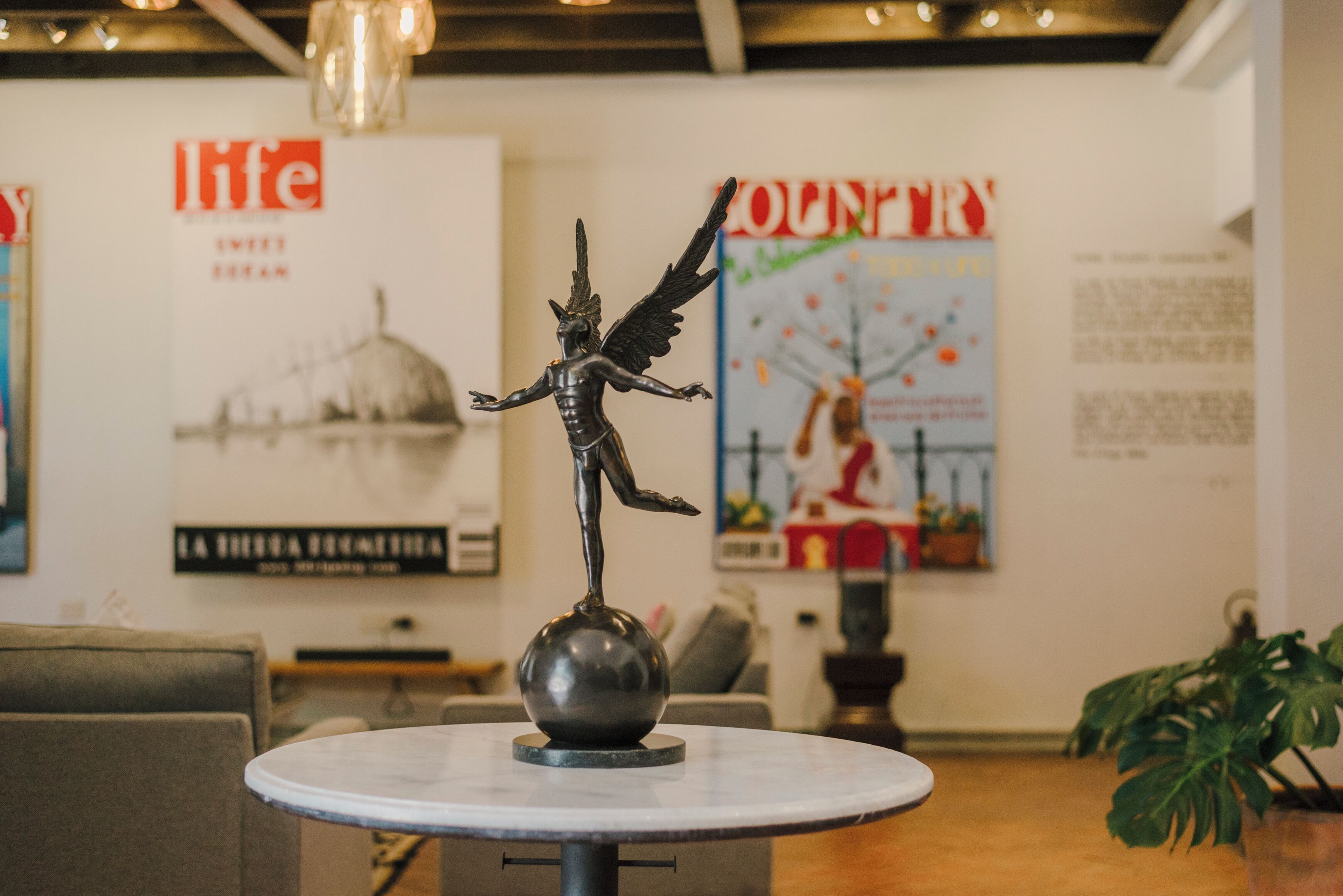 A statue on a table in a room with a poster of a cityscape and a poster of a woman in red.