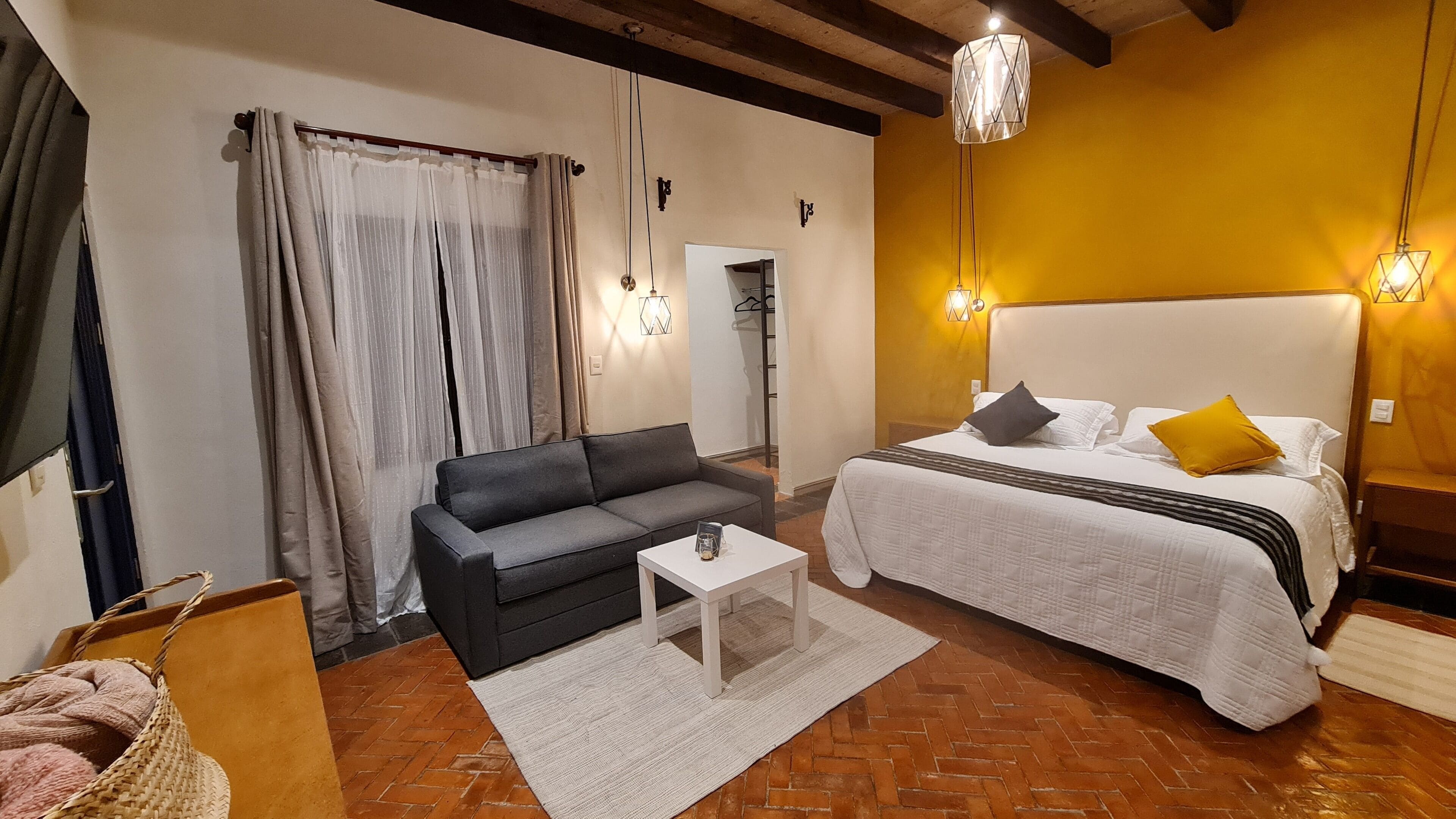 Un dormitorio con cama, sofá, mesa de centro y ventana con cortinas.