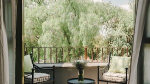 An open balcony with two chairs and a small table, overlooking a lush garden with trees and a clear sky. - Agua Santa Hotel Boutique (San Miguel de Allende)