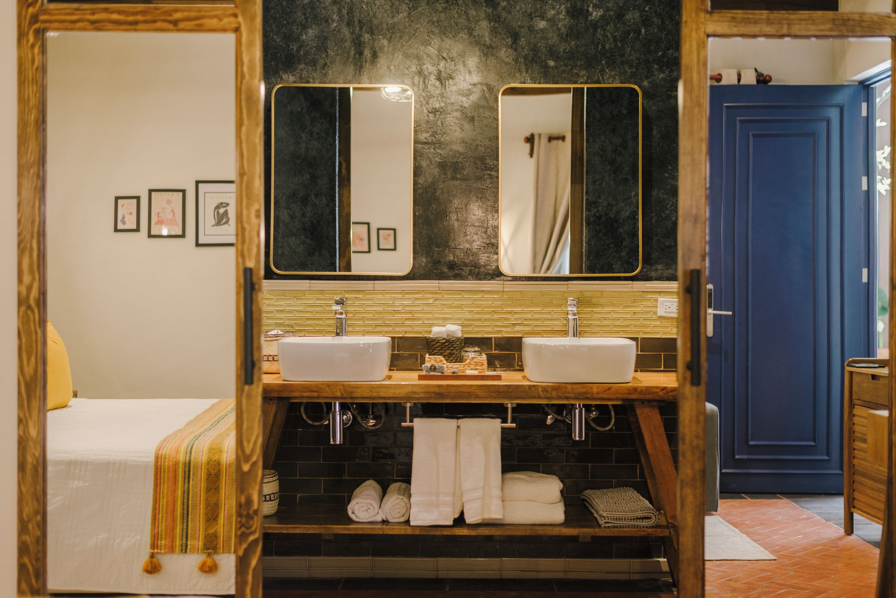 A bathroom with two sinks, a large mirror, and a bed with a striped blanket.