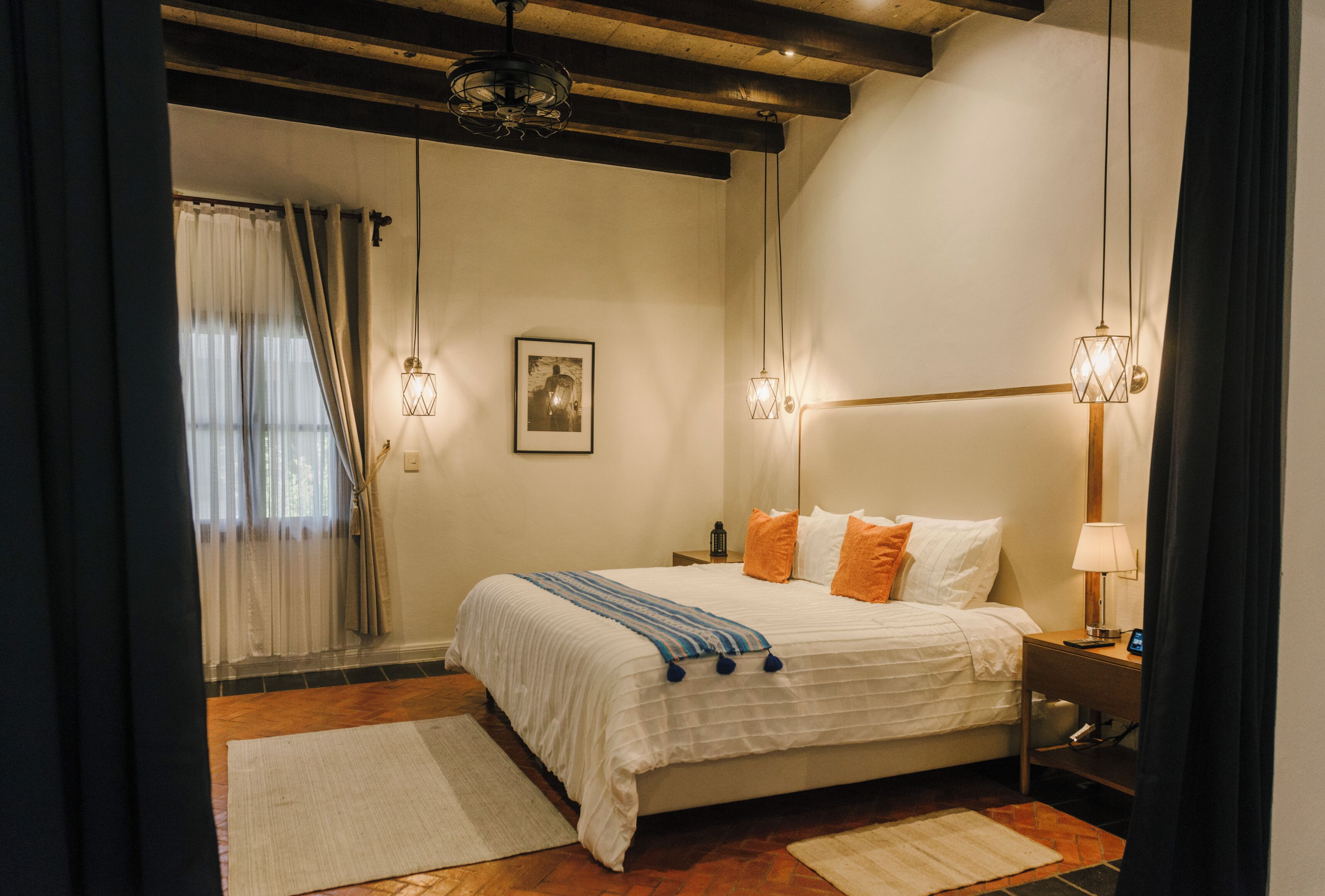 Un dormitorio con una cama, mesitas de noche, una lámpara y un cuadro en la pared.