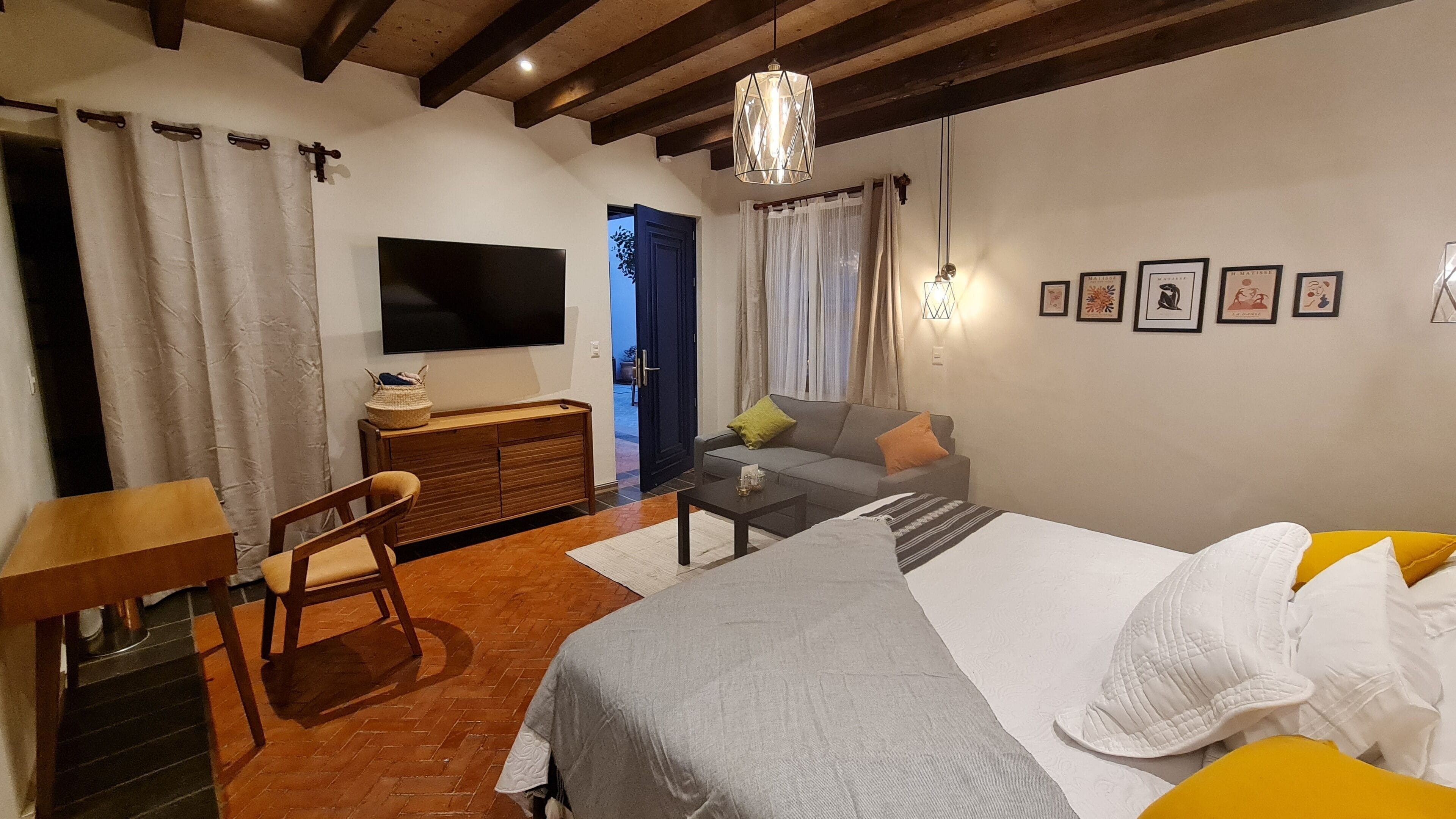 A cozy room with a bed, a desk, a chair, a TV, and a sofa.