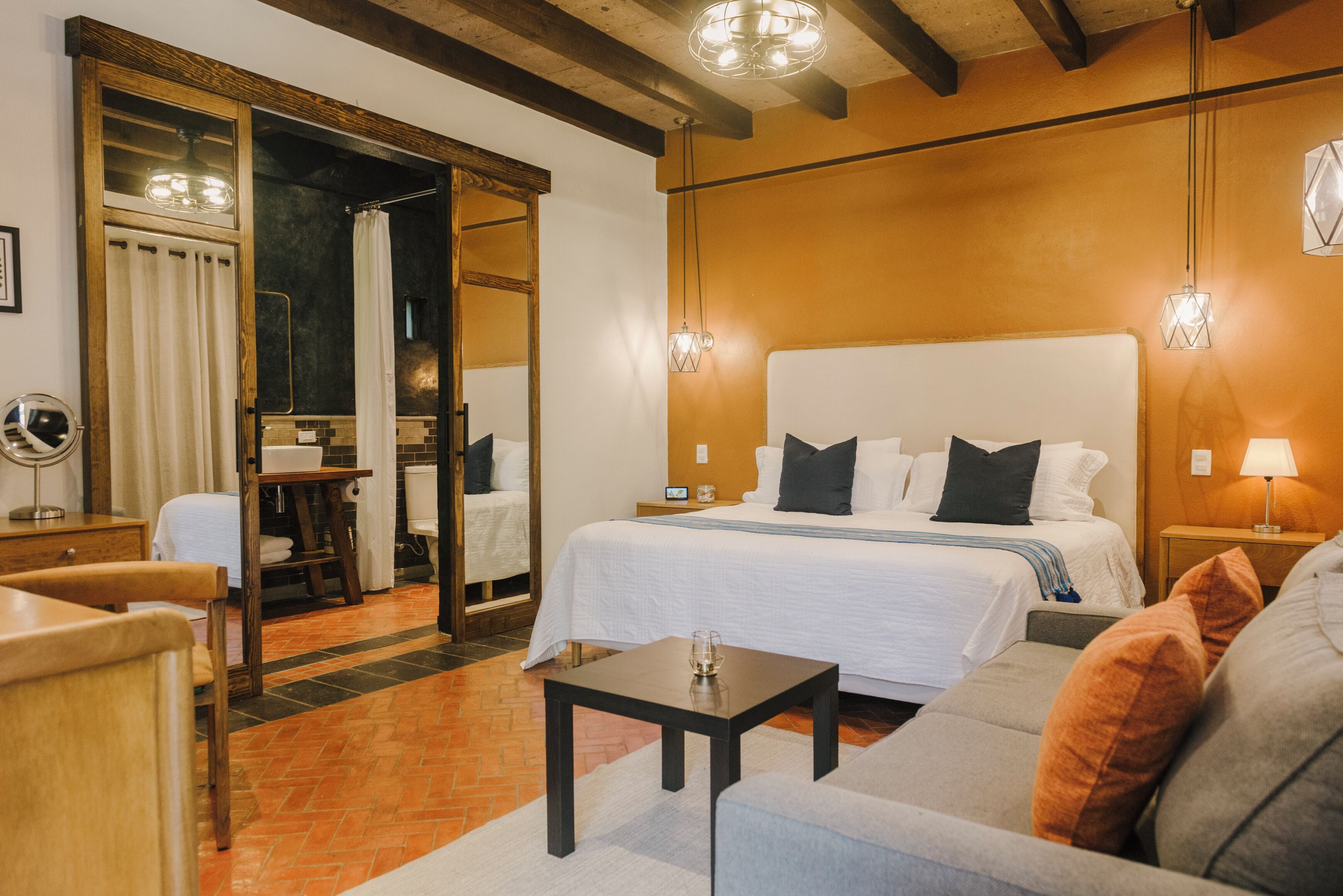 A hotel room with a large bed, a small table, a sofa, and a mirror.